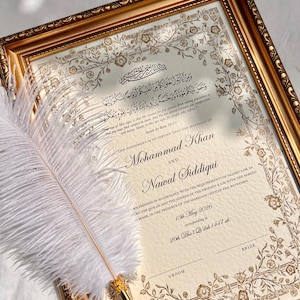 Pode incluir: Um certificado de casamento islâmico emoldurado com bordas florais em folha de ouro e caligrafia árabe. O texto inclui os nomes Mohammad Khan e Nawal Siddiqui, datado de 13 de maio de 2026. Uma pena branca repousa diagonalmente no documento.