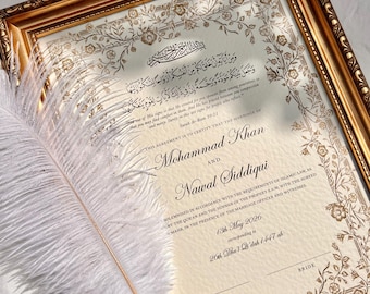 May include: A framed Islamic marriage certificate with gold foil floral borders and Arabic calligraphy. The text includes the names Mohammad Khan and Nawal Siddiqui, dated 13th May 2026. A white feather quill pen rests diagonally across the document.