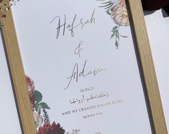 Peut inclure: Impression encadrée de mariage avec les noms "Hafsah & Adam" en lettres dorées et la date "26.06.21". L'impression présente des arrangements floraux bordeaux, crème et verts, et contient un texte du Coran 78:8.
