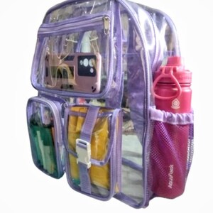 Op de afbeelding: Een transparante paarse rugzak met een zijvak van gaas en een voorvak met ritssluiting. De rugzak heeft een groot hoofdvak en een kleiner voorvak. De rugzak is gevuld met verschillende items, waaronder een waterfles, een telefoon en een notitieboek.