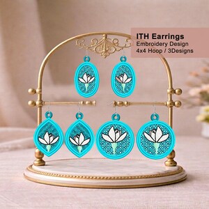 May include: A display of turquoise embroidered earrings with a white flower design, hanging on a gold-colored earring stand. The earrings have different shapes, including oval, teardrop, and circular. The text on the image says "ITH Earrings Embroidery Design 4x4 Hoop / 3 Designs."