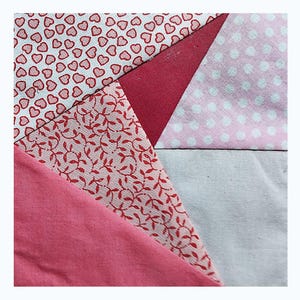 May include: A patchwork of fabric squares in shades of pink and white. The squares feature different patterns, including hearts, leaves, and polka dots.