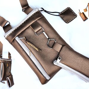 May include: A metallic bronze crossbody bag with a textured finish, featuring a white zipper and a small matching coin purse. The bag has an adjustable strap and a silver-tone metal clasp.