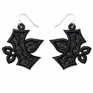 May include: A pair of black embroidered earrings featuring a stylized fleur-de-lis shape with intricate thread detailing and a textured center. Each earring hangs from a silver-toned metal hook, showcasing a symmetrical design with pointed edges.
