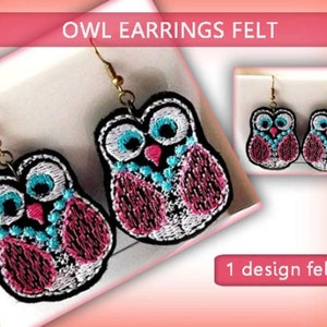 May include: A pair of felt owl earrings with pink, white and blue details. The earrings are on a white background with the text "1 design felted".