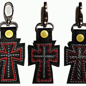 May include: Three black leather keychains with silver clasps. Each keychain features a red and white embroidered cross.