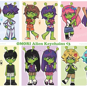 May include: A set of ten colorful cartoon alien keychains. The keychains feature characters with different colored hair, clothing, and accessories. The text "OMORI Alien Keychains <3" is printed at the bottom of the image.