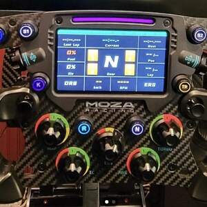 Könnte beinhalten: Ein schwarzes Rennsportlenkrad mit Carbon-Design. Das Lenkrad verfügt über eine Vielzahl von Knöpfen und Drehknöpfen, darunter ein digitales Display, das die aktuelle Geschwindigkeit des Fahrers, den Gang und andere Informationen anzeigt. Das Display zeigt auch den Text "MOZA RACING" an.