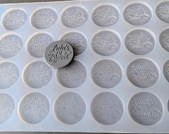 May include: A translucent silicone mould featuring twenty-four circular cavities, each embossed with the text "Lulu's Sweet" in a decorative script font. A single grey circular disc with the same embossed text rests on top of the mould.