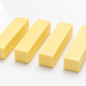 May include: Four rectangular blocks of solid pale yellow material arranged in a parallel row. Each block features a smooth, matte surface with sharp, clean edges and a uniform, consistent color throughout the entire structure of the objects.
