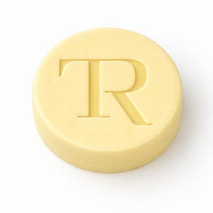 May include: A round, pale yellow object with the letter "R" carved into its surface. The letter is in a serif font and is centered on the object. The object is on a white background.
