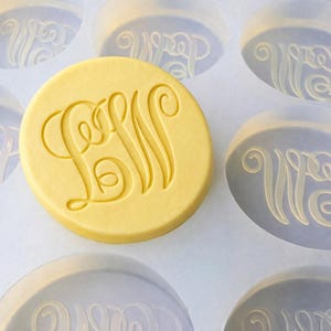 May include: A yellow, circular mold with the embossed letters "LMW" in a decorative script. The mold is surrounded by other similar molds, some with the letters "WP". The design is likely for creating personalized items.