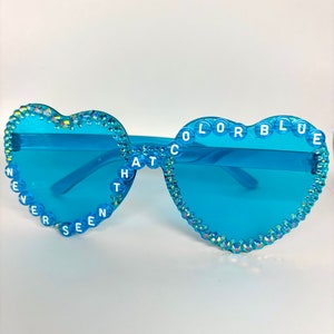 Puede incluir: Gafas de sol azules en forma de corazón con pedrería y las palabras "NEVER SEEN THAT COLOR BLUE" escritas en las monturas.