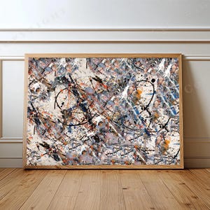 May include: A rectangular wall art piece featuring an abstract expressionist painting with chaotic splatters and drips of black, white, orange, and blue paint on a light beige background, enclosed in a simple light-toned wooden frame.