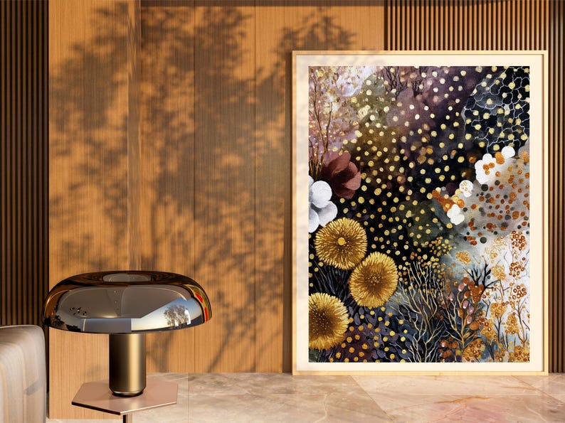 Puede incluir: Una pintura de acuarela enmarcada con un tema floral. La obra de arte presenta un fondo oscuro con puntos dorados y varias flores en tonos de amarillo, blanco y burdeos. La pintura se exhibe sobre una superficie de m&aacute;rmol.