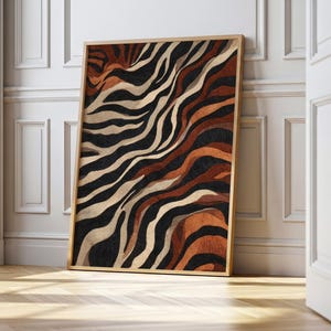 May include: A framed artwork featuring an abstract zebra stripe pattern. The design incorporates black, tan, and brown wavy lines. The artwork is displayed against a white wall and wooden floor.