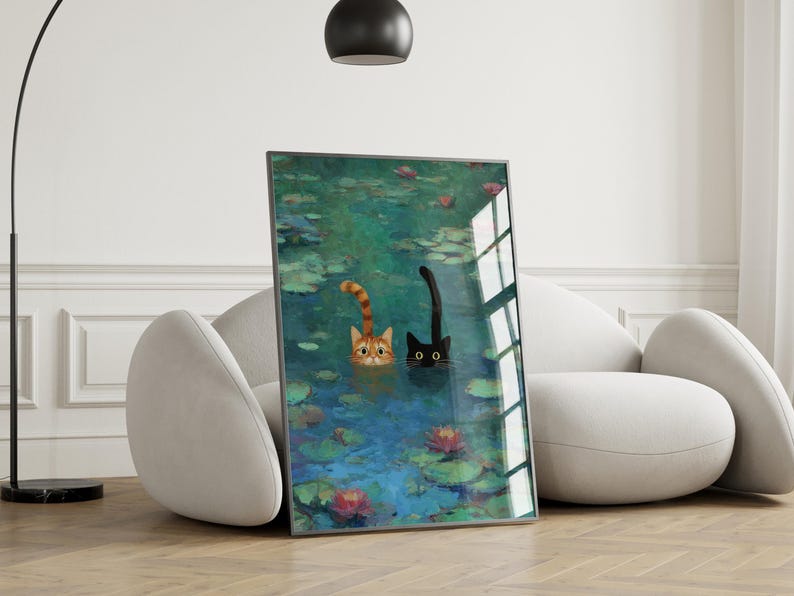 May include: A framed art print depicting two cats in a pond with water lilies. One cat is ginger, the other is black. The artwork is displayed in a modern living room, leaning against a white sofa, creating a stylish interior.
