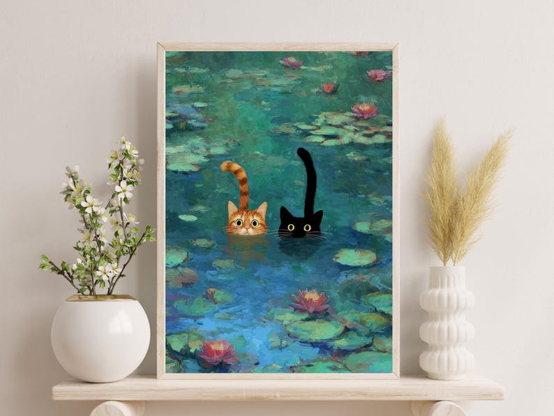 May include: A framed art print showing two cats in a pond with lily pads and flowers. One cat is ginger and white, the other is black. The water is blue and green, and the artwork has a painterly style.