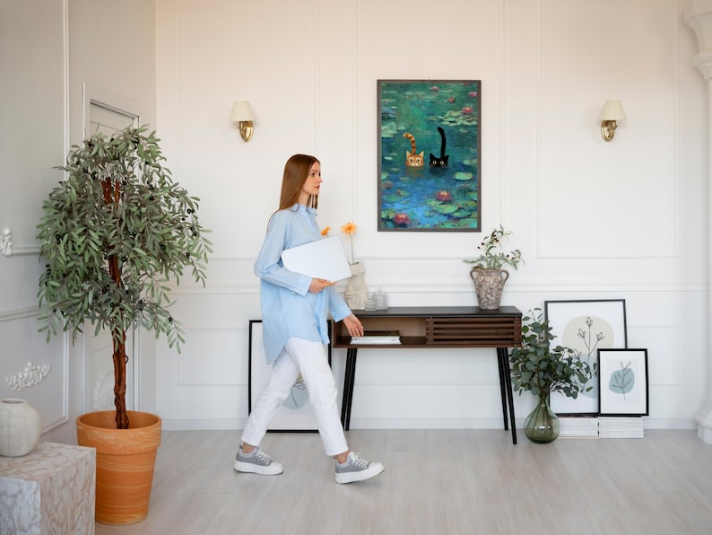 May include: A bright living room with a painting of cats in a pond, a wooden console table, and a large potted tree. The room has white walls, a light wood floor, and wall sconces. A person is walking through the room.