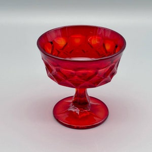 May include: A ruby red glass dessert dish with a diamond pattern on the bowl. The dish has a short stem and a round base. The glass is transparent, allowing light to pass through.