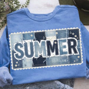 Könnte beinhalten: Hellblaues Sweatshirt mit Jeans-Patchwork-Design. Das Wort "SUMMER" ist in Jeansbuchstaben geschrieben, mit einem weißen, gewellten Rand. Das Design enthält kleine Anker- und Blumendetails.