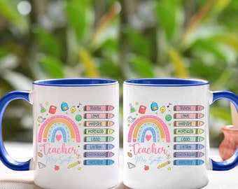 May include: Two white ceramic mugs with blue rims. Both mugs feature a rainbow with a heart at the center, surrounded by colorful crayons and school-themed icons. The text "Teacher" is written below the rainbow, followed by "Mrs. Smith". The crayons have words written on them, including "Teach", "Love", "Inspire", "Motivate", "Lead", "Listen", "Encourage", and "Include".