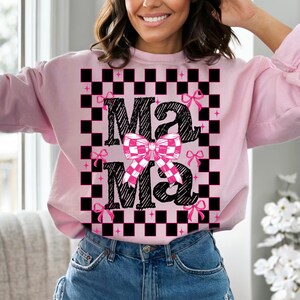 Puede incluir: Sudadera rosa con un patr&oacute;n de cuadros negros y blancos y el texto "Mama" en una fuente de letra negra con lazos rosas.