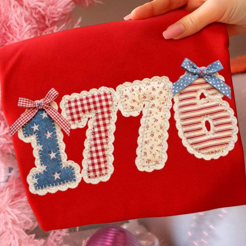 May include: A red fabric item with the numbers "1776" appliqued on the front. The numbers are made from various patterned fabrics, including denim with stars, gingham, floral, and striped patterns. Each number is outlined with a white lace trim and adorned with a bow.