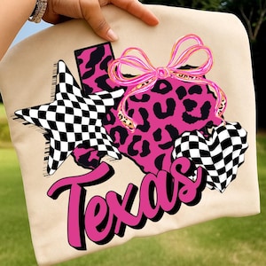 May include: A beige canvas tote bag featuring a graphic of the state of Texas in pink leopard print, adorned with a pink bow. A black and white chequered star and heart are positioned on the sides, with the word Texas in bold pink script.
