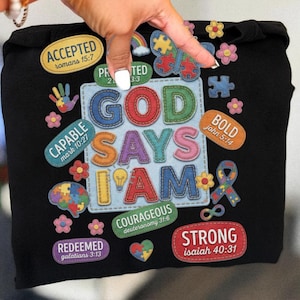 Op de afbeelding: Zwarte hoodie met kleurrijke patches en de tekst "GOD SAYS I AM". Patches bevatten "ACCEPTED", "CAPABLE", "REDEEMED", "BOLD", "COURAGEOUS" en "STRONG", samen met andere afbeeldingen.