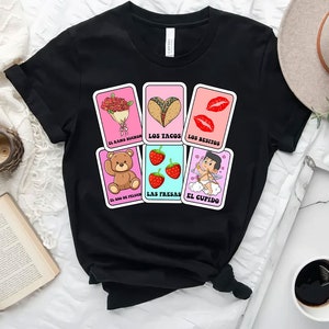 May include: Black t-shirt featuring a design of six colourful cards with illustrations of a bouquet of flowers, tacos, lips, a teddy bear, strawberries, and Cupid. The text on the cards reads "El ramo buch&oacute;n", "Los tacos", "Los besitos", "El oso de peluche", "Las fresas", and "El cupido".