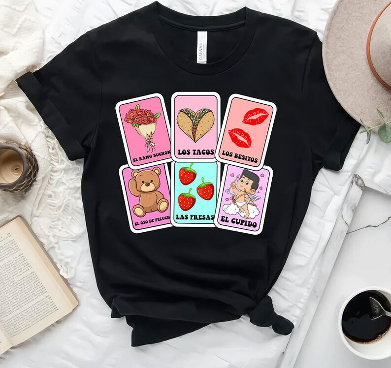 May include: Black t-shirt featuring a design of six colourful cards with illustrations of a bouquet of flowers, tacos, lips, a teddy bear, strawberries, and Cupid. The text on the cards reads "El ramo buch&oacute;n", "Los tacos", "Los besitos", "El oso de peluche", "Las fresas", and "El cupido".