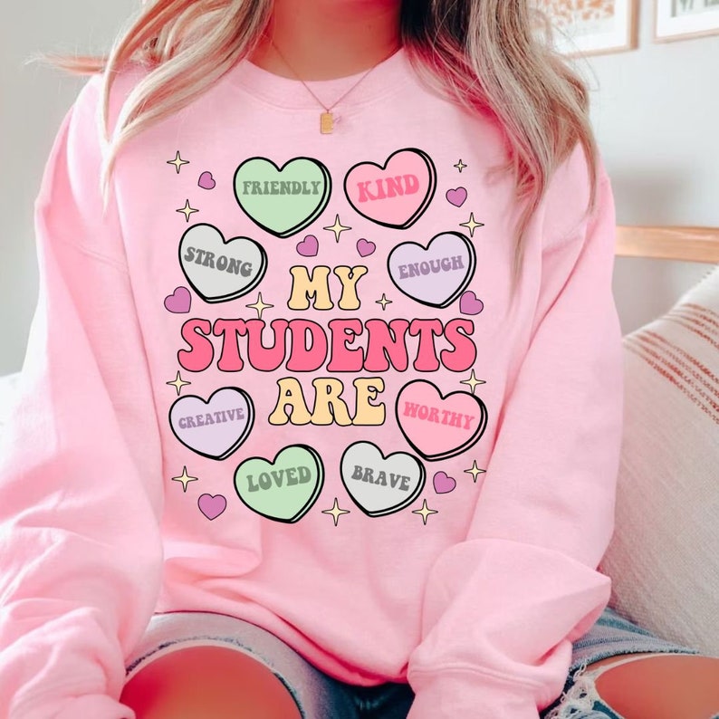 May include: Pink sweatshirt with the text "My Students Are" surrounded by colorful candy hearts with words like "Friendly", "Kind", "Strong", "Enough", "Creative", "Loved", "Brave", and "Worthy".