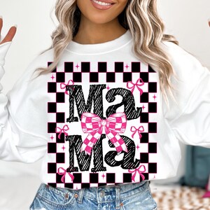 Puede incluir: Sudadera blanca con un patr&oacute;n de cuadros negros y blancos y la palabra "Mama" en negro con un lazo a cuadros rosa y blanco.