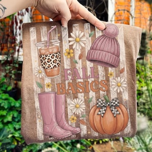 May include: A brown sweatshirt featuring a graphic print with the text FALL BASICS, a leopard print iced coffee cup, a mauve knit beanie, pink rain boots, a pumpkin with a black and white checkered bow, and white daisy flowers.