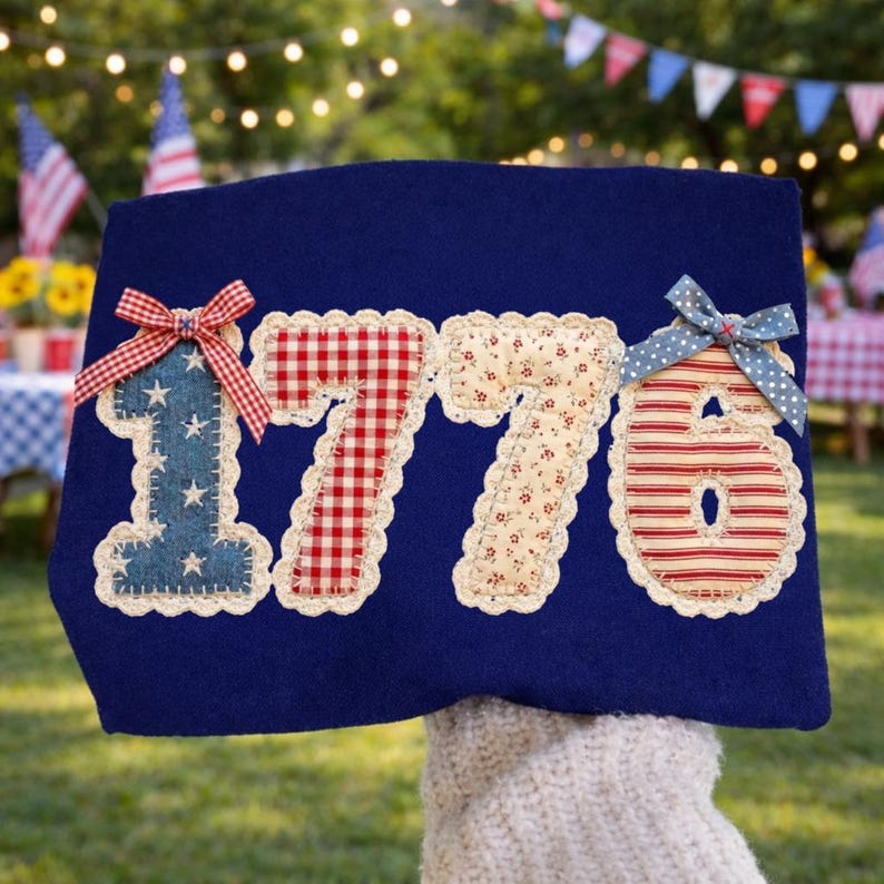 May include: A navy blue fabric decoration with the number "1776" appliqued in various patriotic patterns. The "1" is blue denim with white stars, the "7"s are red gingham and floral, and the "6" is red and white striped. Each number has a decorative bow.