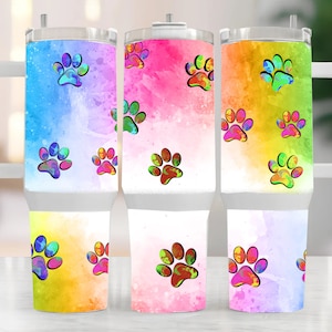 Op de afbeelding: Drie roestvrijstalen bekers met witte handvatten en deksels. Elke beker heeft een kleurrijke aquarel achtergrond met pootafdruk ontwerpen. De achtergronden zijn in tinten blauw, roze en geel met bijpassende pootafdrukken.