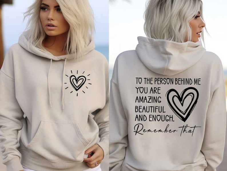 May include: A beige hoodie with a black heart design on the front and the text "TO THE PERSON BEHIND ME YOU ARE AMAZING BEAUTIFUL AND ENOUGH. Remember that" on the back.