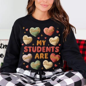 May include: Black sweatshirt with the text "MY STUDENTS ARE" in gold and red letters. The sweatshirt features heart-shaped designs with words like "Friendly", "Kind", "Strong", "Creative", "Loved", and "Brave".