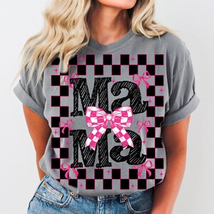 Puede incluir: Camiseta gris con un patr&oacute;n de cuadros blanco y negro y la palabra "Mama" escrita en negro con un lazo rosa en el centro.