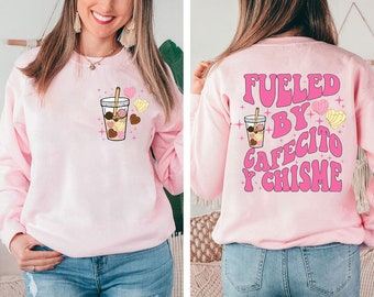 May include: Pink sweatshirt with a graphic of a coffee cup with pastries and the text "Fueled by Cafecito y Chisme" in pink letters.