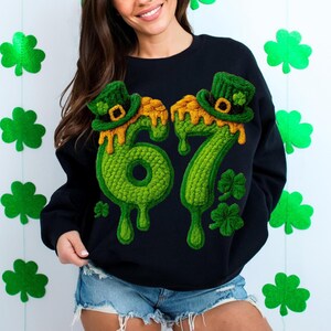 May include: Black sweatshirt with a green and gold embroidered design featuring the numbers "67" with melting gold accents, green leprechaun hats, and shamrocks. The sweatshirt is a St. Patrick's Day theme.