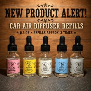 May include: Five glass dropper bottles of car air diffuser refills labeled Saddle Up Beard Care. Each 0.5 oz bottle features a different colored label: pink, yellow, white, blue, and grey. Text reads NEW PRODUCT ALERT! CAR AIR DIFFUSER REFILLS.