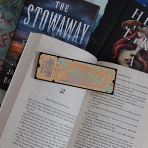 Könnte beinhalten: Nahaufnahme eines geöffneten Buches mit dem Titel "The Stowaway" auf dem Cover. Das Buch ist auf Seite 21 aufgeschlagen, und der Text "Server Down, Server Down" ist sichtbar. Das Buch ist von anderen Büchern umgeben, darunter eines mit dem Titel "Her Dark Lies".