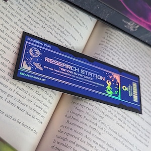 May include: A blue and iridescent boarding pass with the text "Research Station" and "Testing My Patience." The pass features a spacecraft, an alien, and the words "Escape Spacecraft."