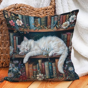 Op de afbeelding: Een witte kat slaapt op een plank vol boeken. De plank is versierd met bloemen en wijnstokken. De kat ligt opgerold op de plank, met zijn kop op zijn poten. De boeken zijn allemaal van verschillende grootte en kleur, en sommige hebben zichtbare titels. De achtergrond is donkergroen.