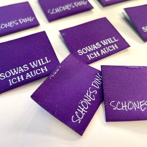 Könnte beinhalten: Lilafarbene Stoff-Etiketten mit weißem Text. Die Etiketten sagen "Schönes Ding" und "Sowas will ich auch".