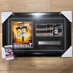 May include: A black framed movie poster with a photo of Mark Wahlberg in the movie Invincible. The poster is signed by Mark Wahlberg and Vince Papali. The poster is in a black frame with a white mat.