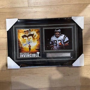 May include: A black framed photo collage featuring two images from the movie "Invincible". The top image shows Mark Wahlberg as Vince Papale running down a street. The bottom image shows Vince Papale in his Philadelphia Eagles uniform. The text "Mark Wahlberg" and "Vince Papale" are printed below the images. The title of the movie "Invincible" is printed in large letters below the top image.