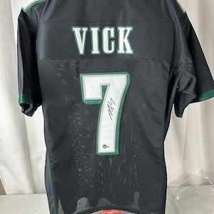 Könnte beinhalten: Schwarzes und grünes Footballtrikot mit dem Namen "VICK" und der Nummer "7" auf der Rückseite. Das Trikot ist mit einem schwarzen Stift signiert.
